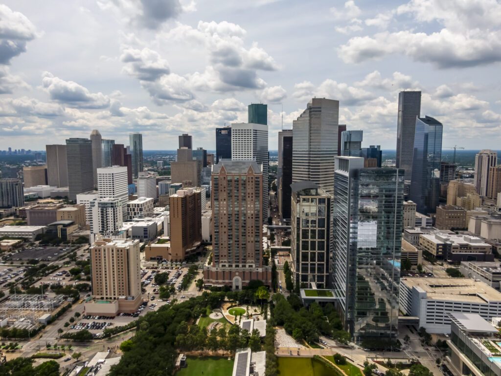 Aerial view of downtown Houston towers and green parks under a summer sky