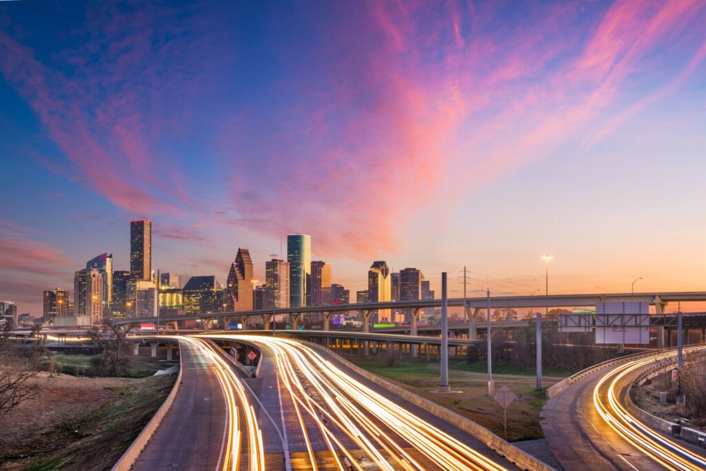 Downtown Houston skyline at dusk under a pink and violet sky, with freeway light trails