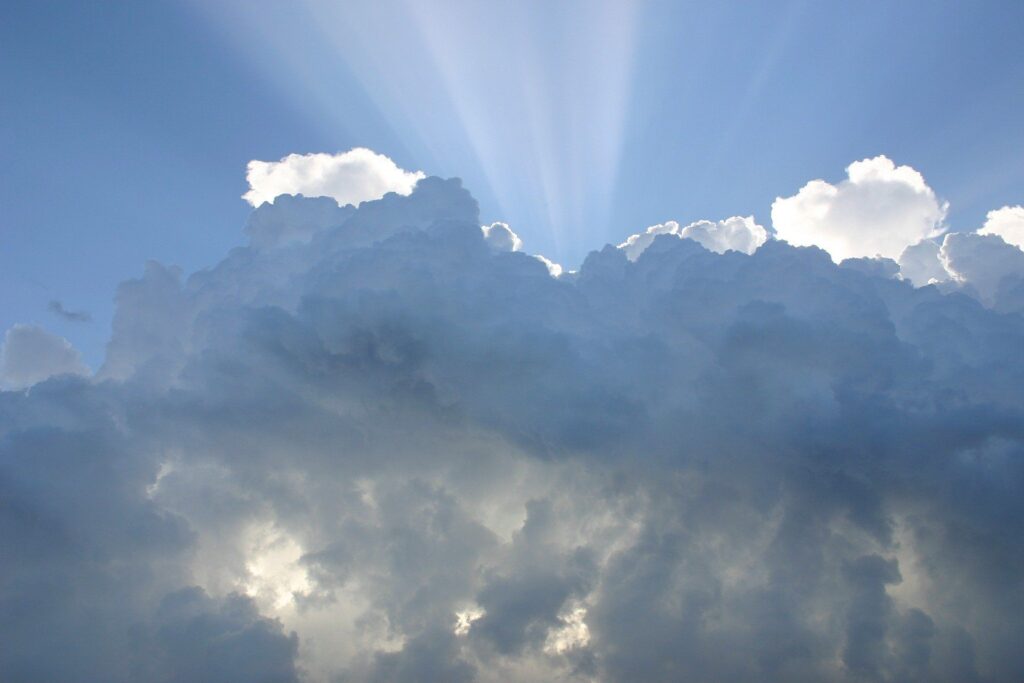 Sunbeams breaking through tall white clouds in a blue sky